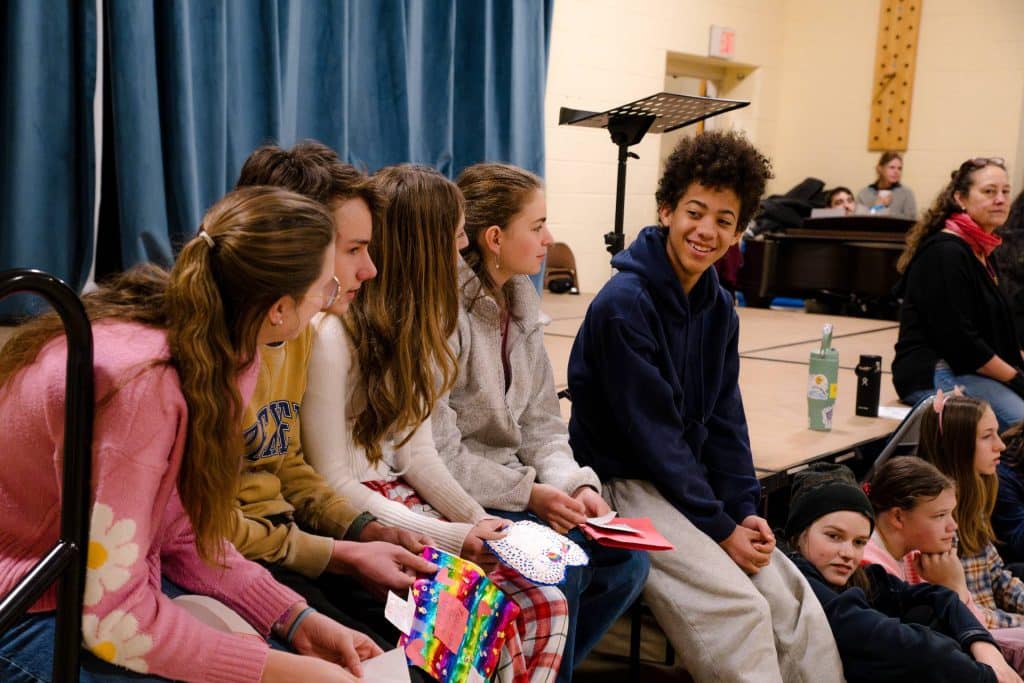 8th graders sitting on the edge of a stage during valentine's day exchange