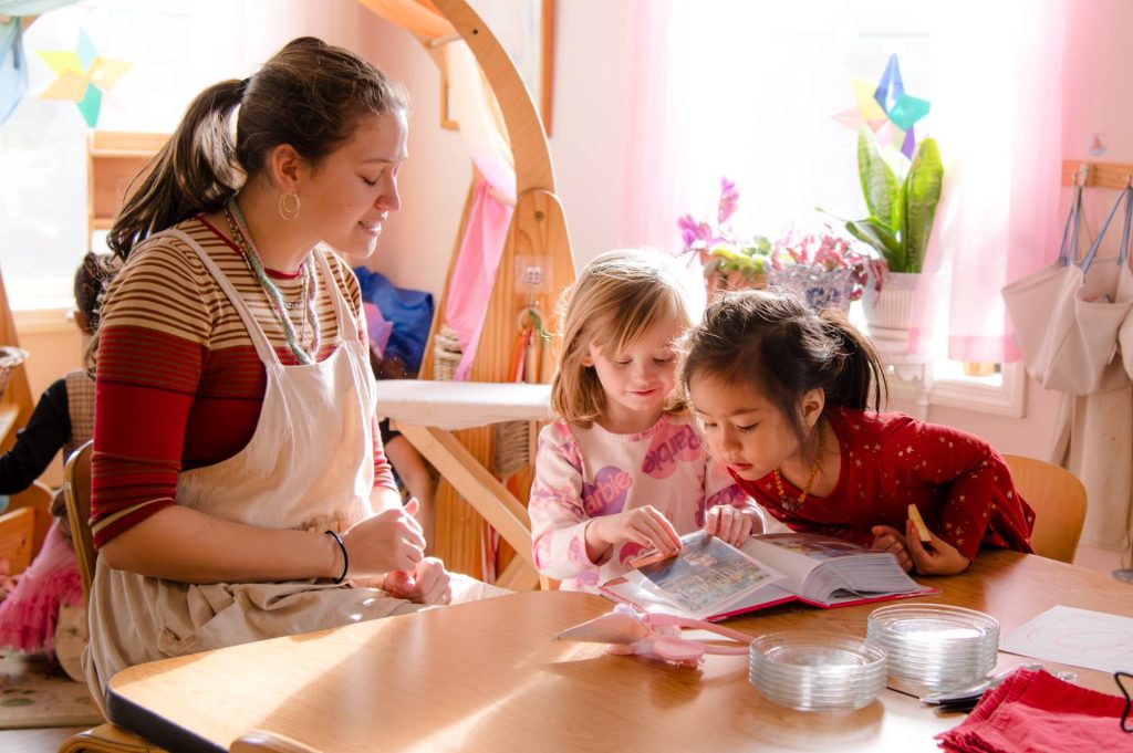 two female early childhood students sitting at a table with their teacher