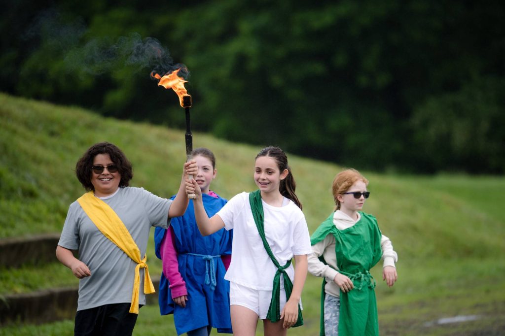 fourth and fifth grade students holding a lighted torch, dressed in tunics during pentathlon