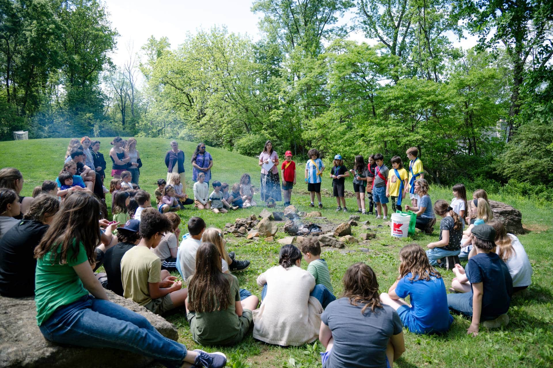 entire river valley waldorf student body sitting around a fire outside in a green field