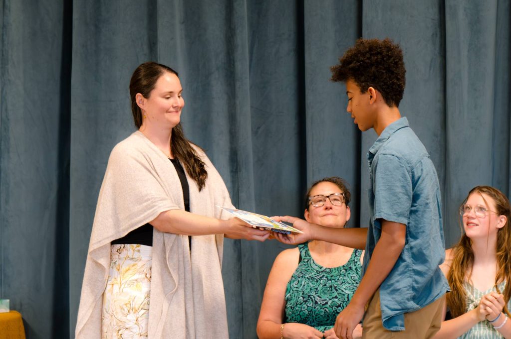 8th grade boy receiving diploma from teacher on stage at graduation