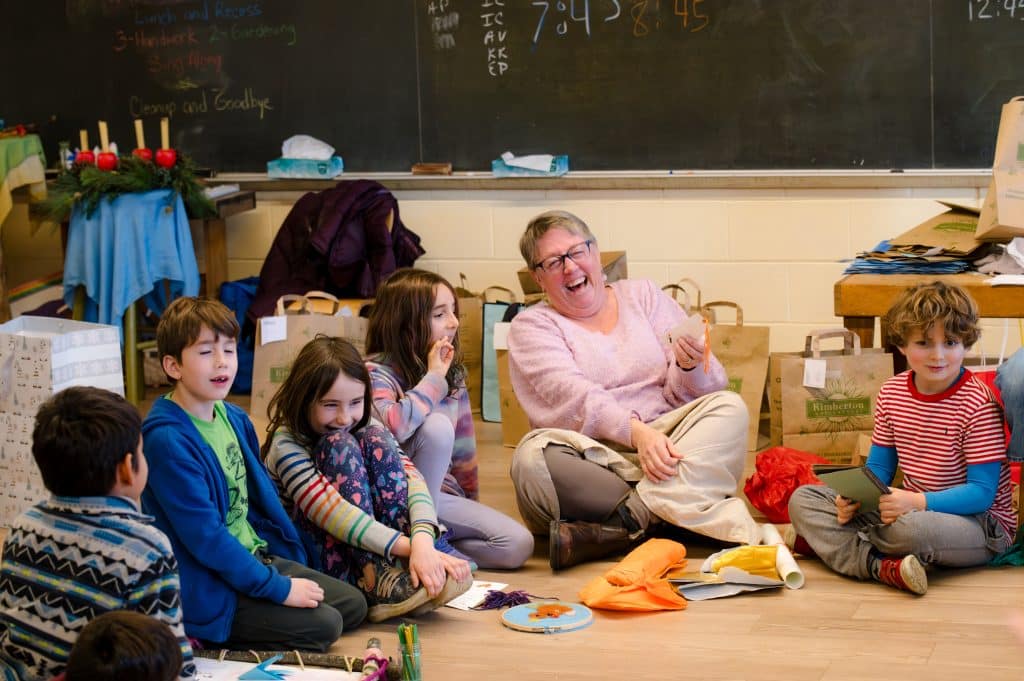 group of 2nd and 3rd graders sitting on the floor laughing with teacher
