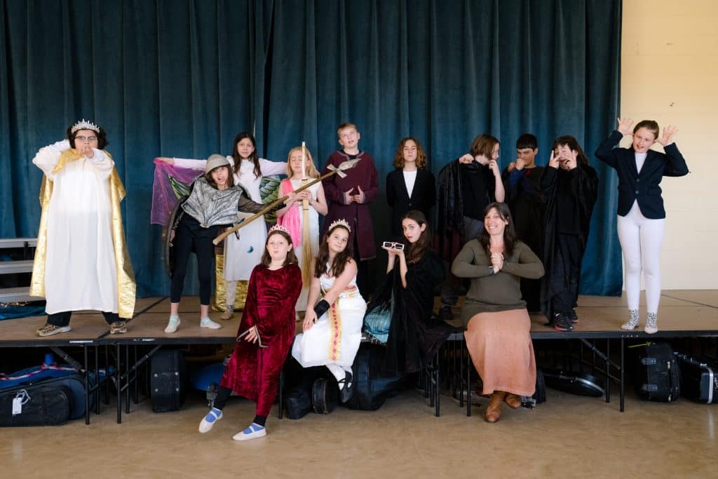 fourth and fifth graders on stage making fun faces after a dress rehearsal