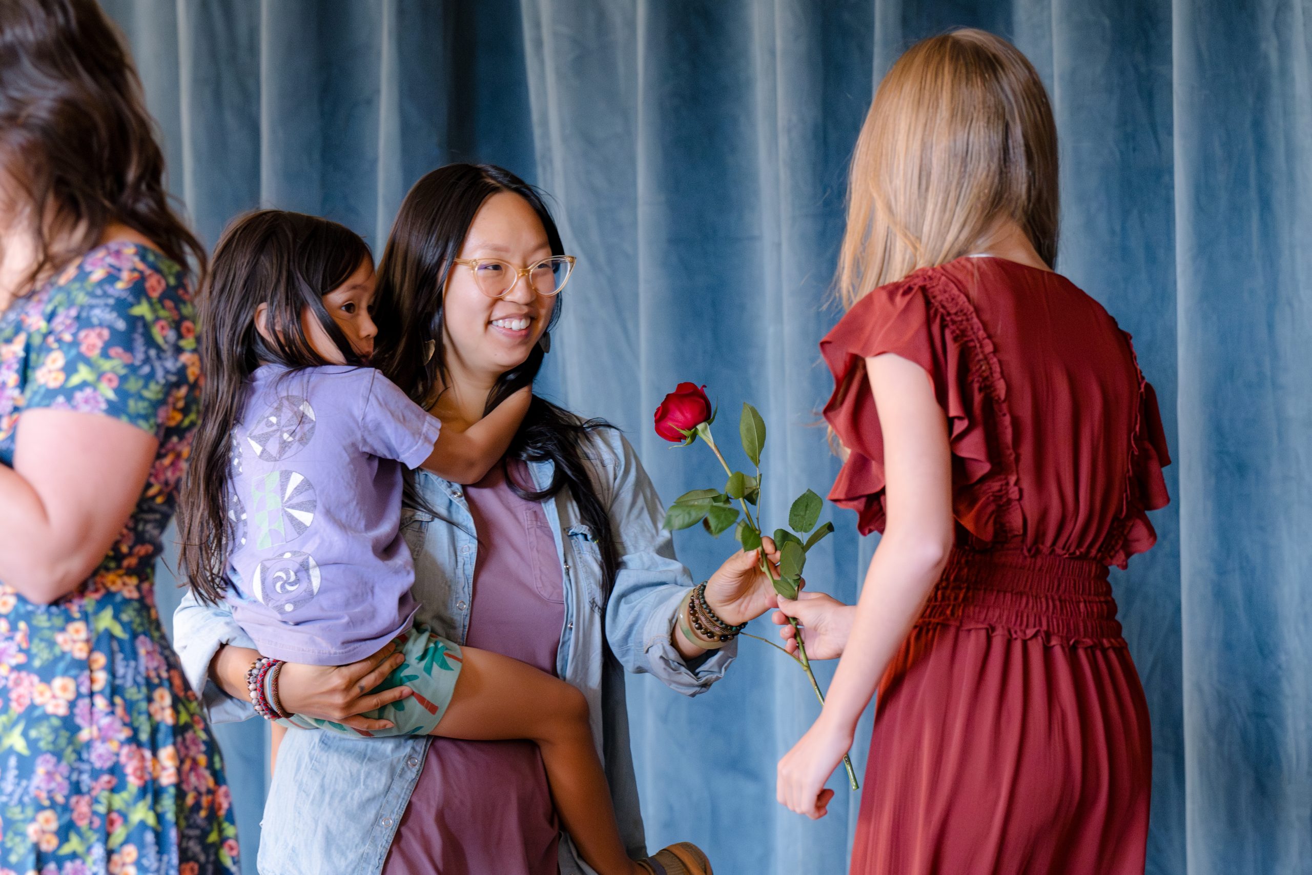 student handing a rose to teacher who is holding a child in her arms