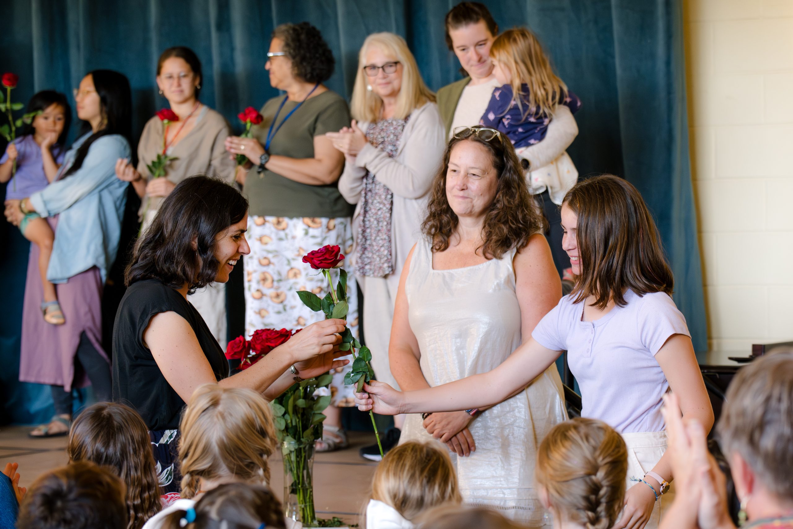 student giving rose to teacher during rose ceremony with many teachers on stage in background