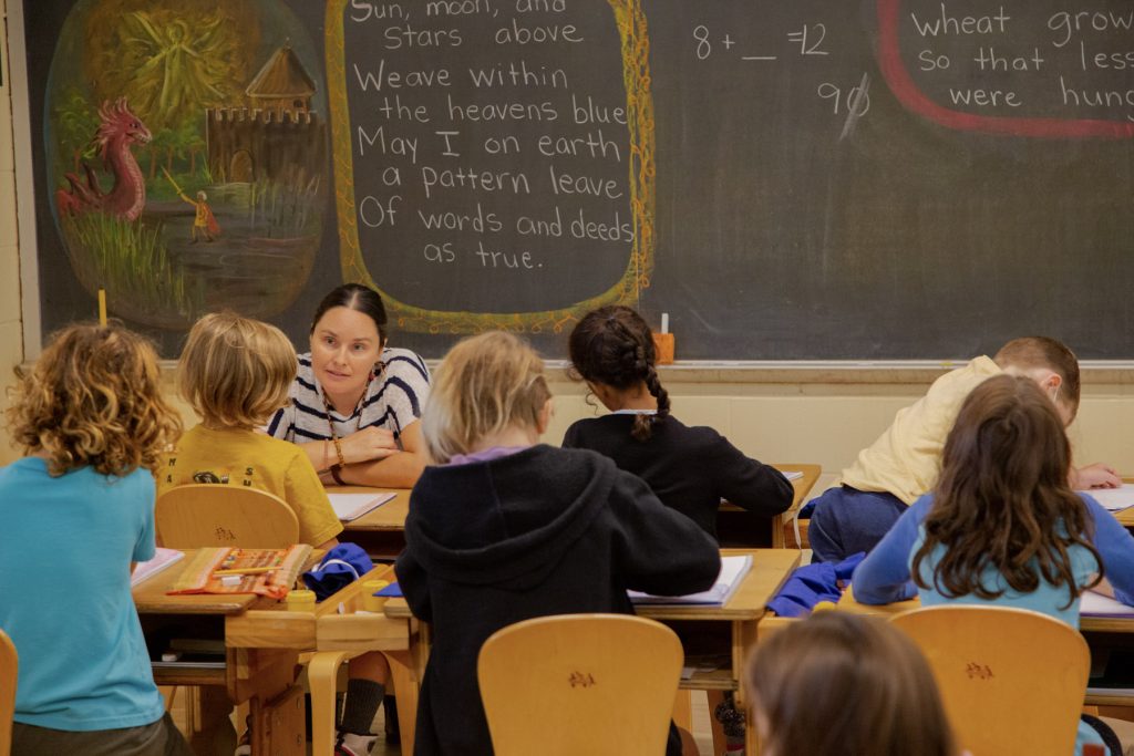 lower grades class in classroom, teacher sitting at the front with students at their desks