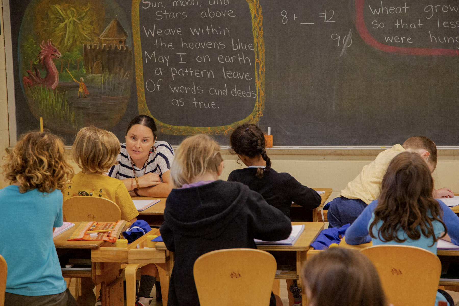 lower grades class in classroom, teacher sitting at the front with students at their desks