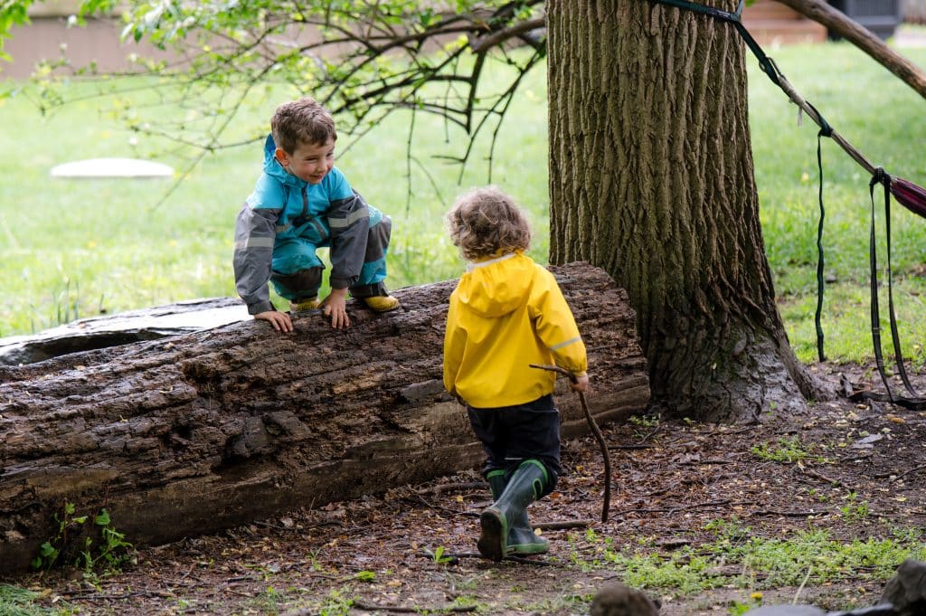 two early childhood boy students playing on a fallen tree outdoors