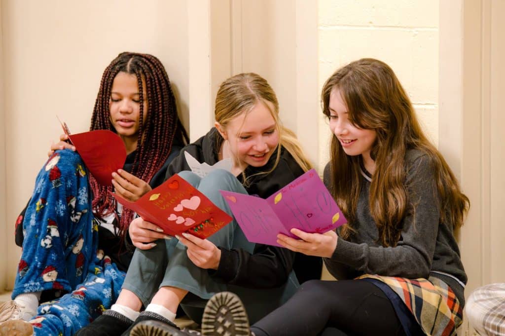 three lower grades or middle school female students sitting next to each other reading cards