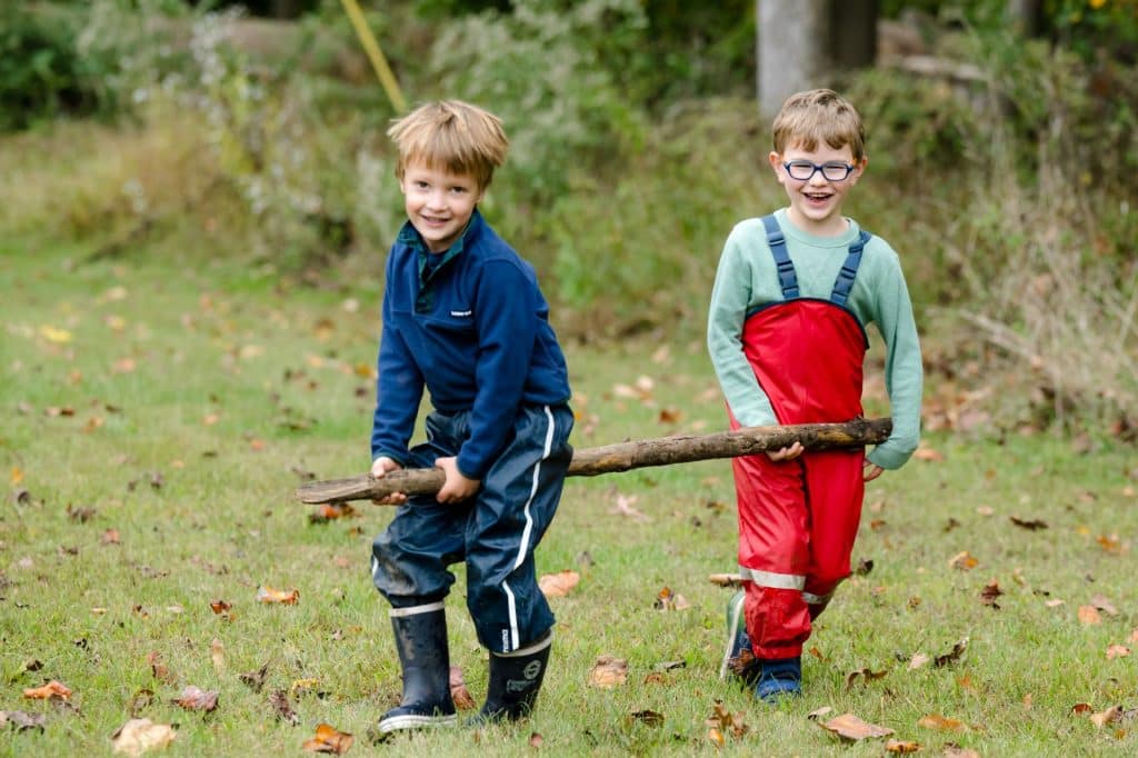 two boys carrying a log and smiling at the camera