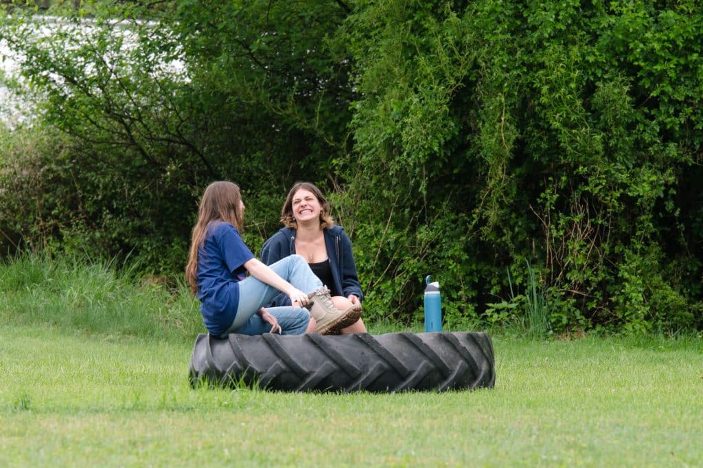 teacher and student sitting on a large tire in a grassy field