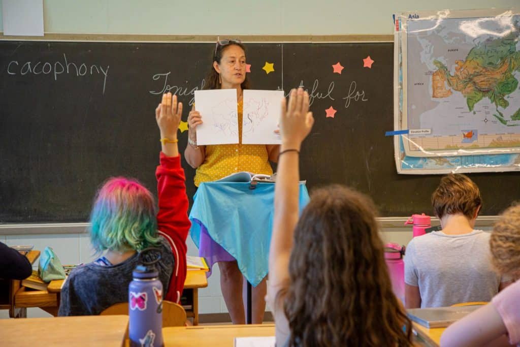 teacher teaching a geography lesson while students raise their hands